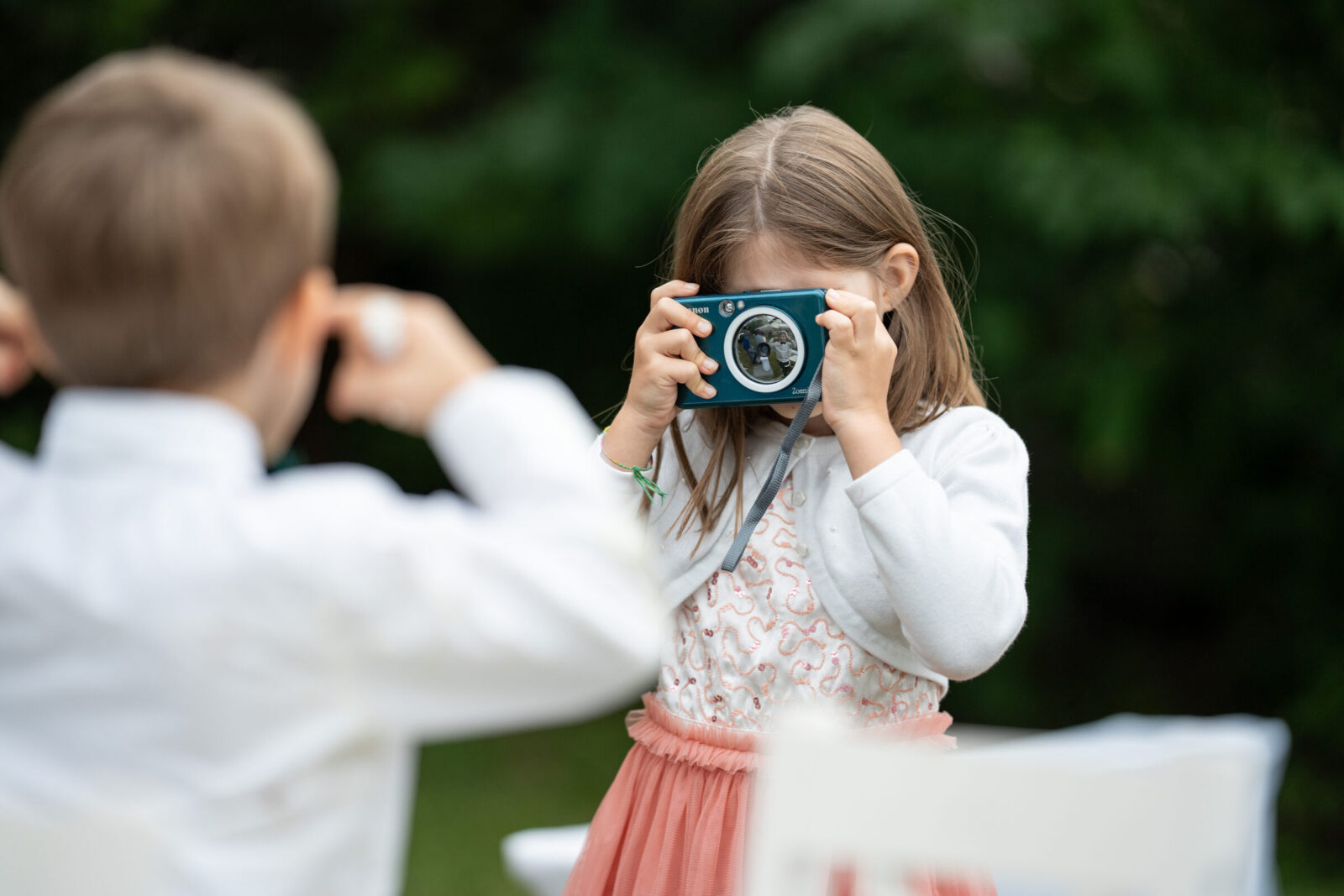 Mädchen fotografiert mit einer kleinen Kamera, ein Bub schaut zu